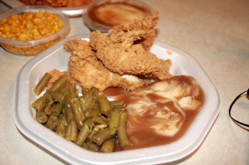 A plate of fried chicken with green beans, corn, and gravy on a white styrofoam tray.