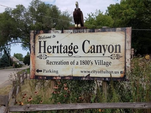 Sign welcoming visitors to Heritage Canyon, a recreation of a 1800s village, with parking information.
