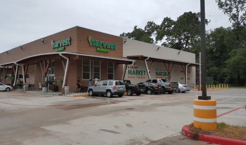 Exterior of Harvest Market with a parking lot, featuring a brick building and green signage on a cloudy day.