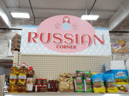 Sign for "Russian Corner" with shelves displaying various Russian food products and condiments.