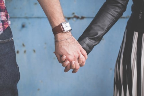 A close-up of two hands holding each other, one wearing a watch, against a blue textured background.