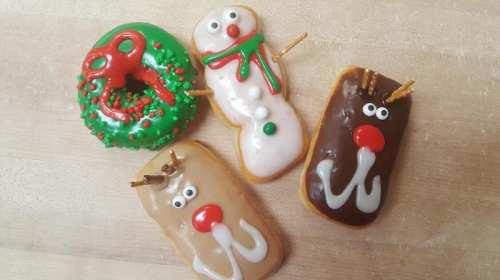 Four festive donuts: a wreath, a snowman, and two reindeer, all decorated with colorful icing and candy.