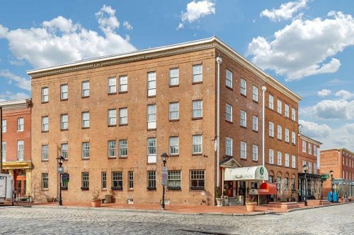 A brick building with multiple windows, featuring a restaurant entrance and a cobblestone street under a blue sky.