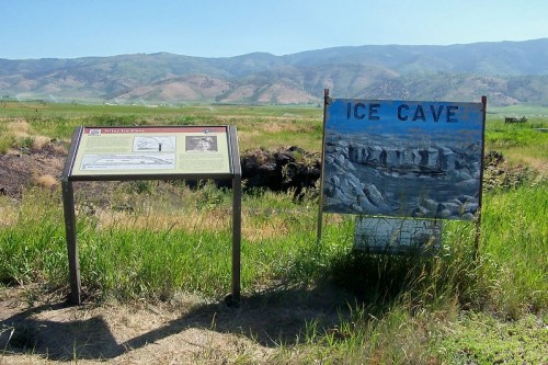Signage for an ice cave, with a painted sign and informational panel, set against a mountainous landscape.