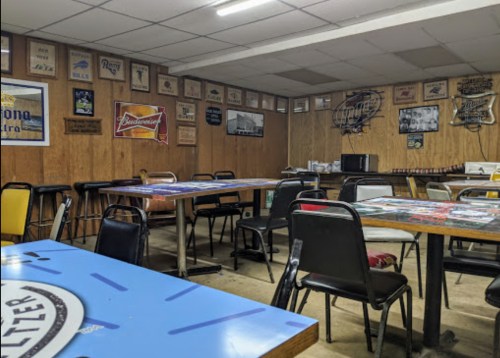 A dimly lit room with wooden walls, tables, and chairs, decorated with vintage beer signs and memorabilia.