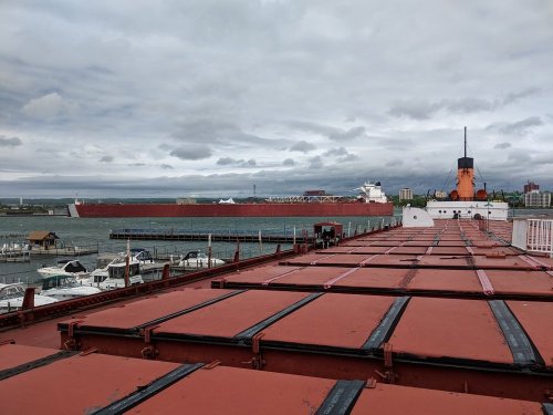 A view from a ship's deck showing a large cargo vessel in the distance under a cloudy sky.