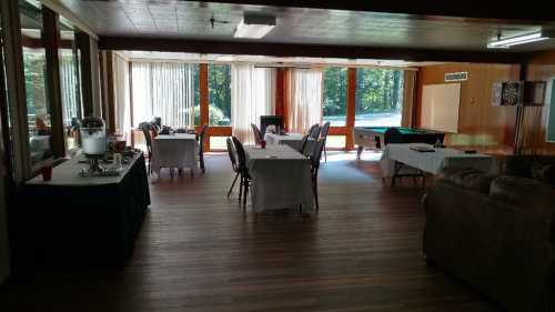 A spacious room with tables set for dining, large windows, and a view of greenery outside.