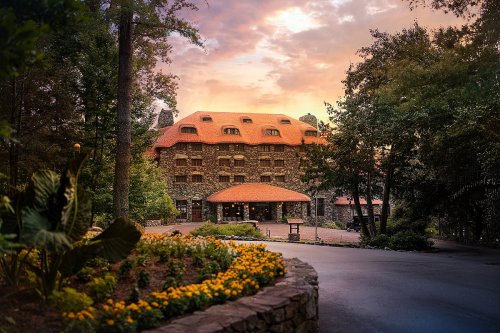 A stone building with a red roof surrounded by trees and colorful flowers at sunset.
