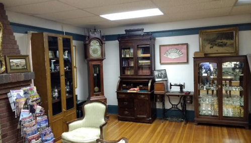 A cozy room filled with antique furniture, including a clock, bookshelves, and display cabinets, on wooden flooring.