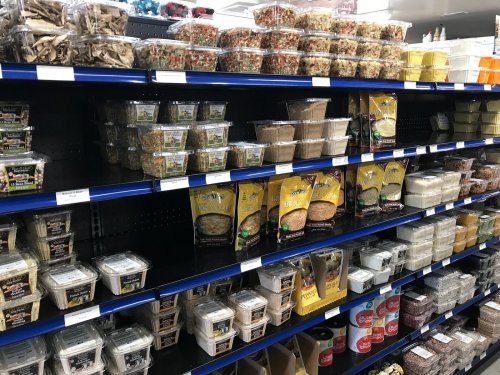 A grocery store shelf filled with various packaged food items, including salads, snacks, and prepared meals.
