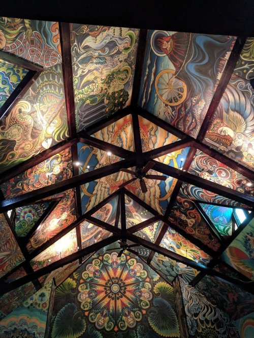 Colorful, intricate murals adorn the ceiling of a building, featuring swirling patterns and vibrant designs.