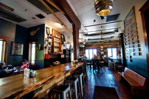 A cozy restaurant interior with wooden decor, a long bar, and patrons enjoying their meals at tables.