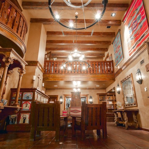 A spacious, rustic interior with wooden beams, a large chandelier, and a dining area featuring wooden furniture.