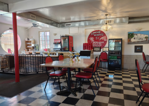 A retro diner interior with checkered floors, red chairs, and a vintage sign on the wall.