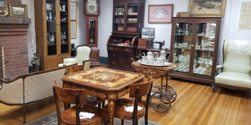 A vintage room featuring antique furniture, a wooden table, chairs, a display cabinet, and a cozy seating area.