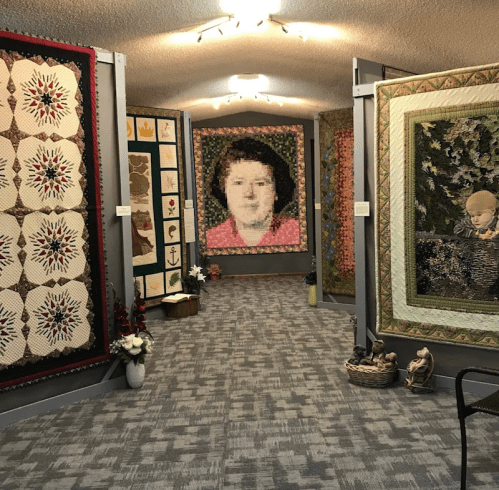 A gallery featuring various quilts on display, including a large quilted portrait and decorative wall hangings.
