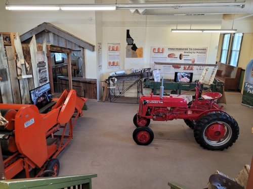 A vintage red tractor and orange farm equipment displayed in a museum with agricultural posters on the walls.