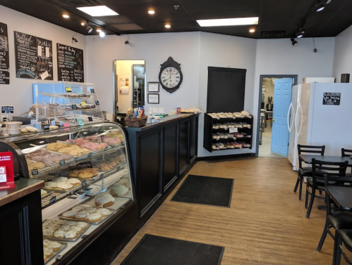 A cozy bakery interior featuring a display case of pastries, a seating area, and a blue door in the background.