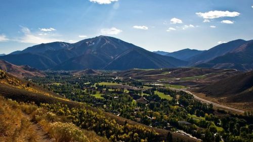 A panoramic view of mountains and valleys under a clear blue sky, with lush greenery and winding roads below.