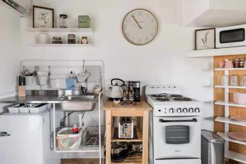 A modern kitchen featuring a sink, stove, clock, and organized shelves with various kitchen items.