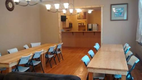 A spacious dining area with wooden tables, blue chairs, and a kitchen in the background. Warm, inviting atmosphere.