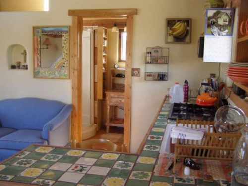 Cozy kitchen and living area with a blue couch, tiled counter, and wooden accents, featuring a glimpse of a bathroom.