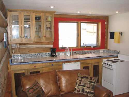 Cozy kitchen with wooden cabinets, a tiled countertop, and a window overlooking the outdoors. A brown couch is nearby.