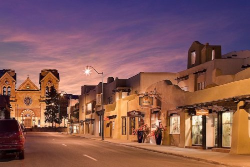 A charming street at dusk, featuring adobe buildings and a historic church in the background, with soft purple skies.