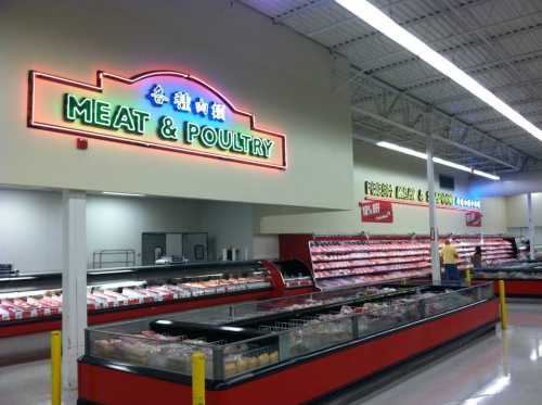 A grocery store meat and poultry section with neon signage and refrigerated displays filled with various meats.