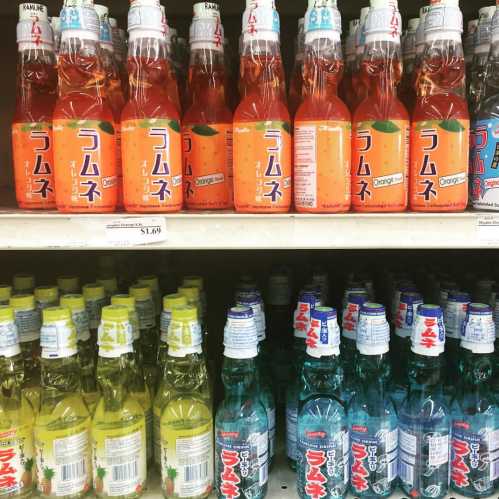 A shelf displaying various colorful bottles of Japanese soda, including orange and blue flavors.