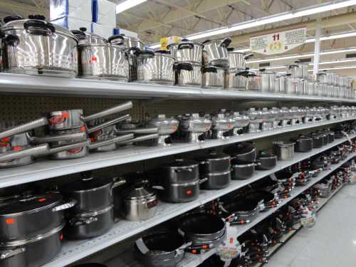 A store shelf filled with various stainless steel pots and pans, neatly arranged in rows.