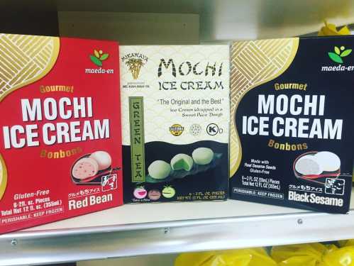 Three boxes of gourmet mochi ice cream bonbons in flavors: red bean, green tea, and black sesame, displayed on a shelf.