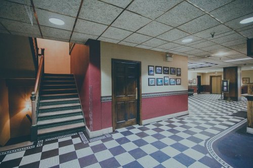 Interior view of a hallway with a staircase, framed photos on the wall, and a patterned floor.