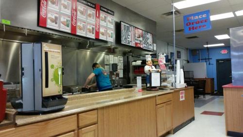 A fast-food restaurant counter with a worker preparing food, menus displayed, and a sign that says "Place Order Here."