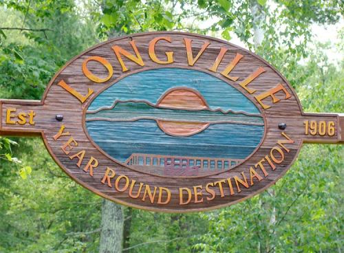 Wooden sign for Longville, established 1906, featuring a scenic design and the text "Year Round Destination."