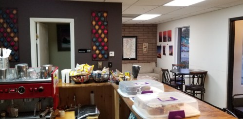 Cozy café interior with a coffee machine, snacks, and seating area featuring colorful wall art.