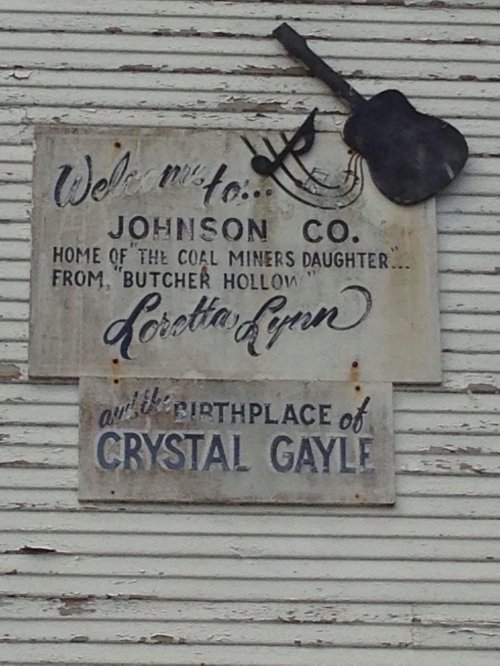 Sign welcoming visitors to Johnson County, home of Loretta Lynn and birthplace of Crystal Gayle, with a guitar decoration.