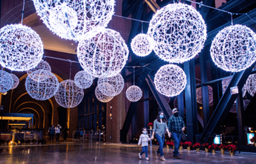 A family walks through a festive space adorned with large, glowing spherical lights during the holiday season.