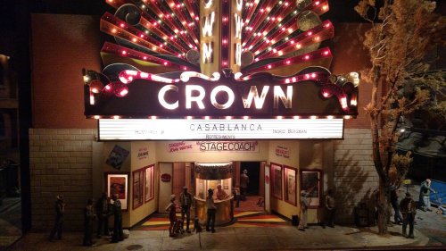 A vintage theater marquee reading "CROWN" with movie posters and people outside, illuminated at night.