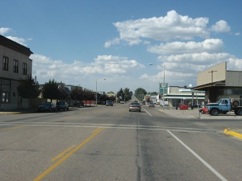 A quiet street scene with cars, buildings, and a blue sky filled with clouds.