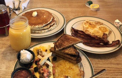 A breakfast spread featuring pancakes, eggs, bacon, toast, and a glass of orange juice.