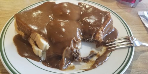 A plate of dessert featuring a chocolate-covered cake with a fork beside it, sitting on a wooden table.