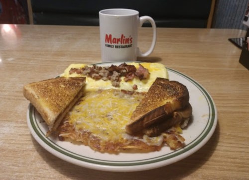 A plate of breakfast featuring an omelet, cheesy hash browns, and toasted bread, with a coffee mug in the background.