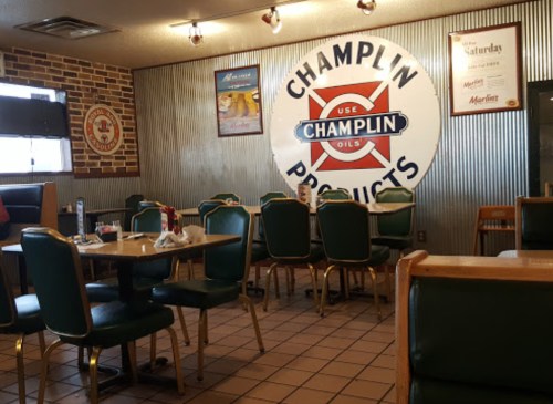 Interior of a diner featuring wooden tables, green chairs, and a Champlin Products sign on the wall.