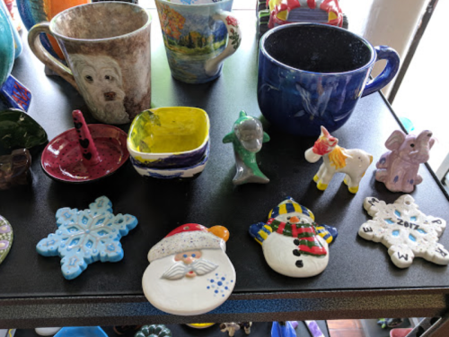 A display of colorful ceramic items, including mugs, figurines, and holiday-themed decorations on a black table.