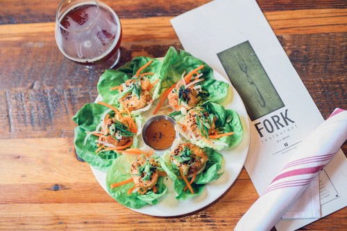 A plate of shrimp lettuce wraps with vegetables, served with a dipping sauce, alongside a drink and a restaurant menu.