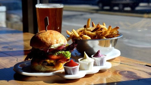 A delicious burger with lettuce and cheese, served with fries and dipping sauces, alongside a glass of beer.