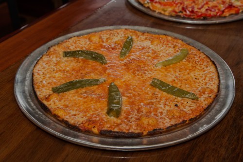 A round pizza with a golden crust, topped with melted cheese and green chili peppers arranged in a star pattern.