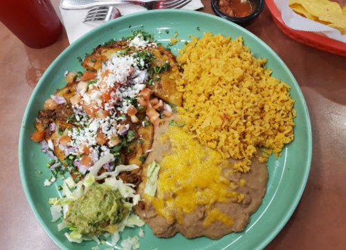 A colorful plate of enchiladas topped with cheese, tomatoes, and cilantro, served with rice, refried beans, and guacamole.