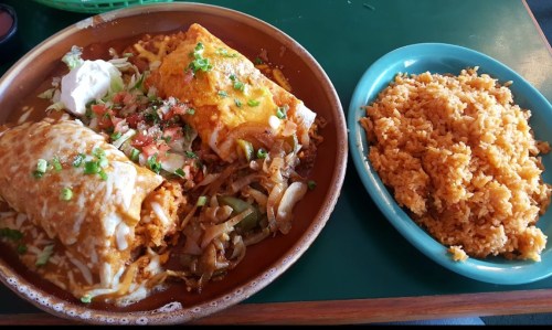 A plate of enchiladas topped with cheese, sour cream, and salsa, served with a side of fluffy rice.